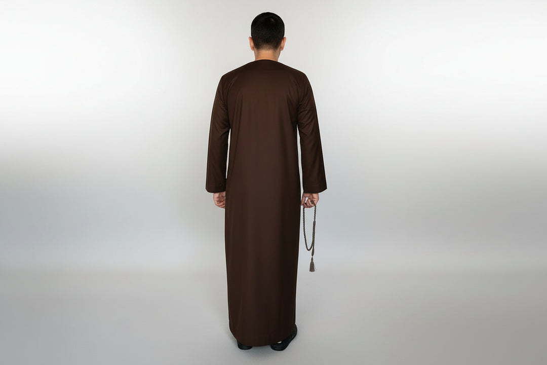 Man wearing a long brown robe holding a prayer mat on a white background